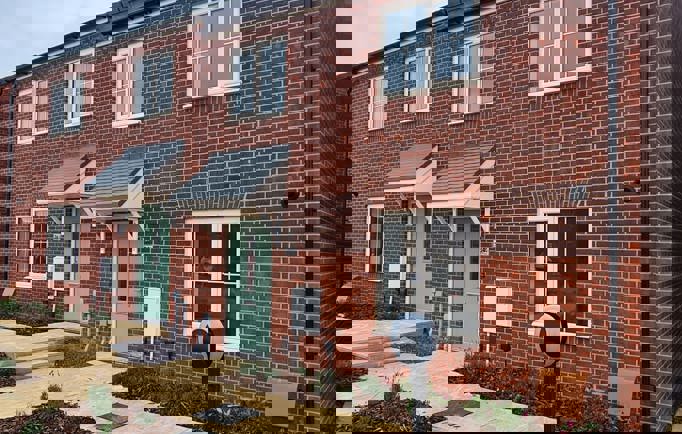 A two-storey red brick housing development with a sage-coloured front door and newly planted flower beds